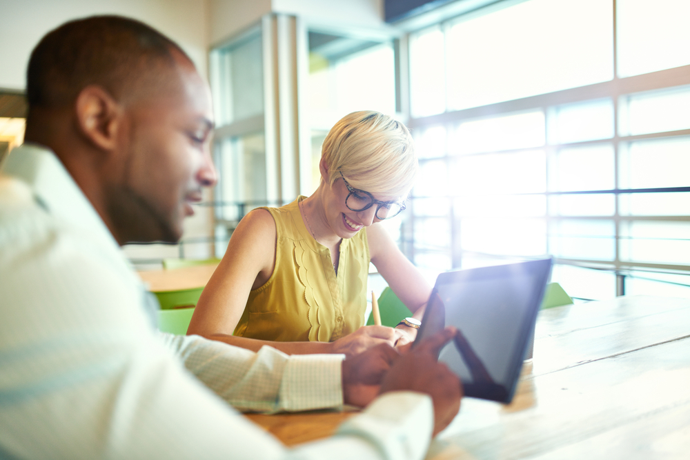 Two creative millenial small business owners working on social media strategy using a digital tablet while sitting at desk-1